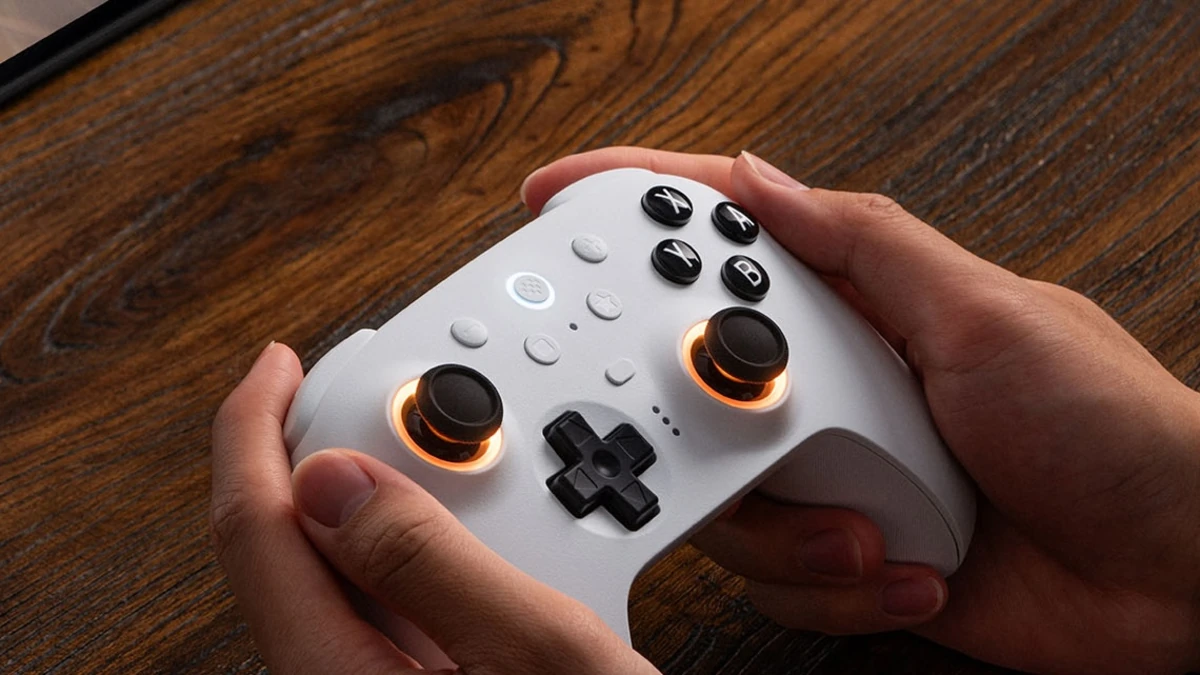 Manos sujetando un 8BitDo Ultimate blanco con anillos naranjas en los sticks