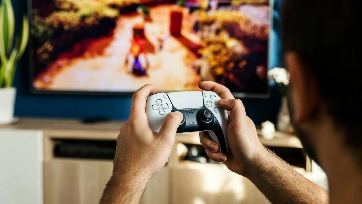 Manos sujetando un DualSense blanco frente a un televisor con un juego