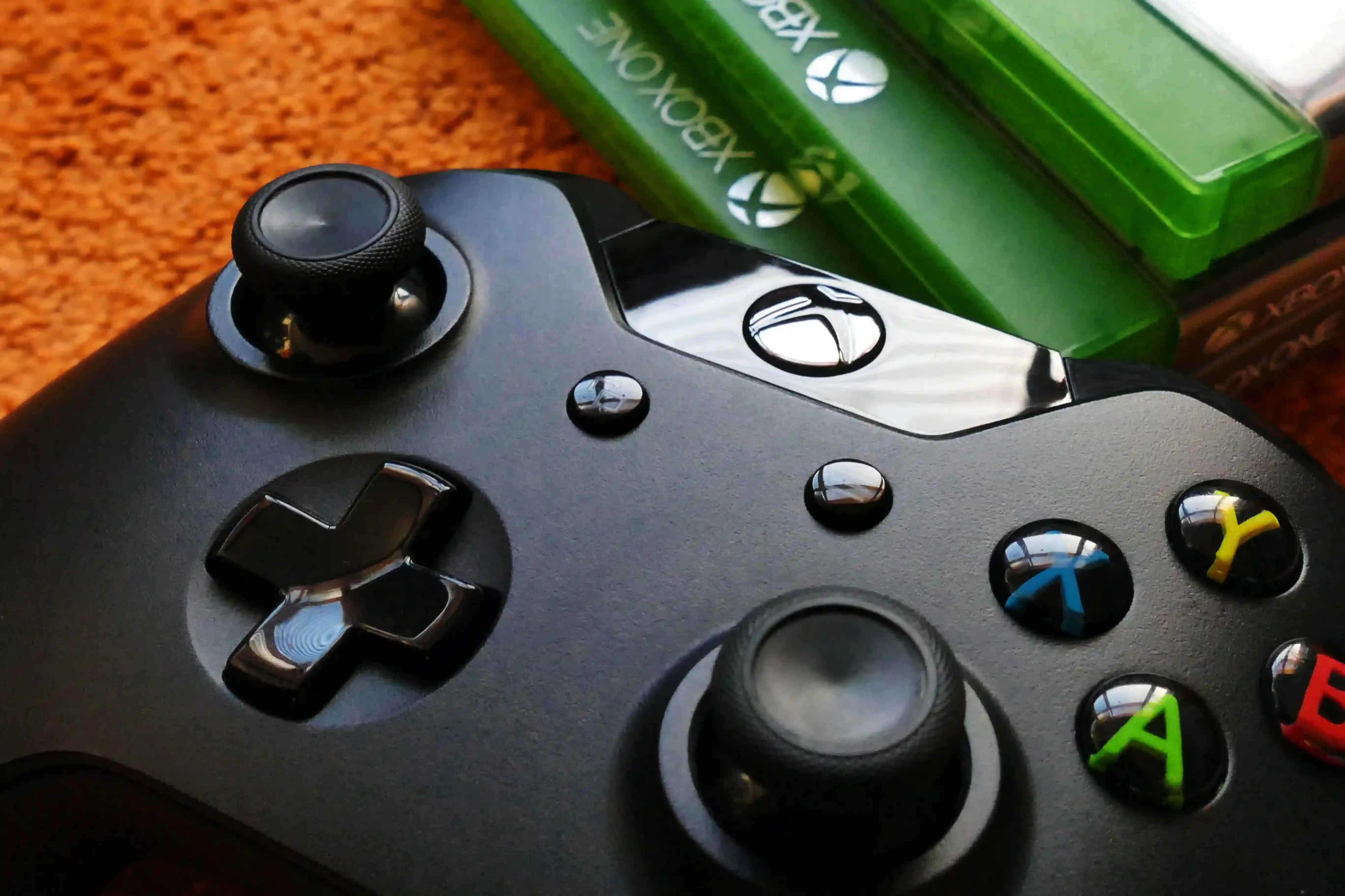 Black Xbox controller on an orange rug with Xbox game cases in the background