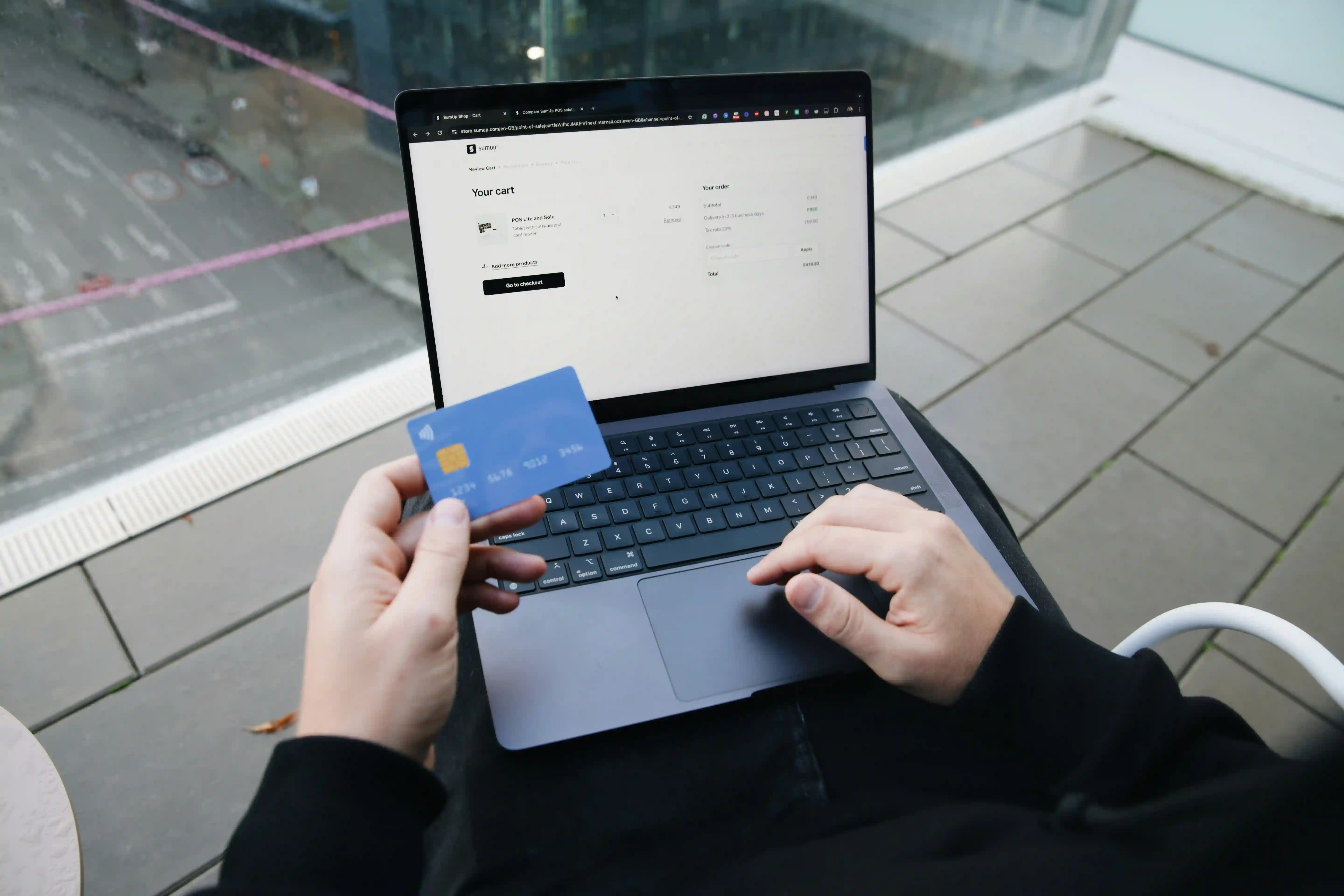Person holding a credit card over a laptop showing an online shopping cart